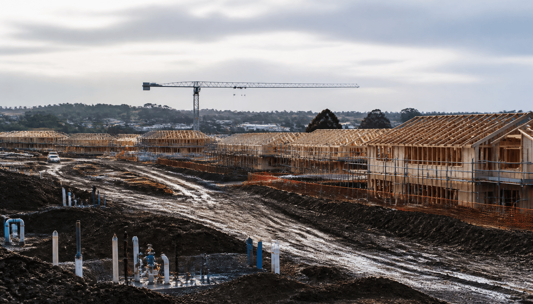 Auckland fringe housing development with unfinished roads and water infrastructure under grey morning sky