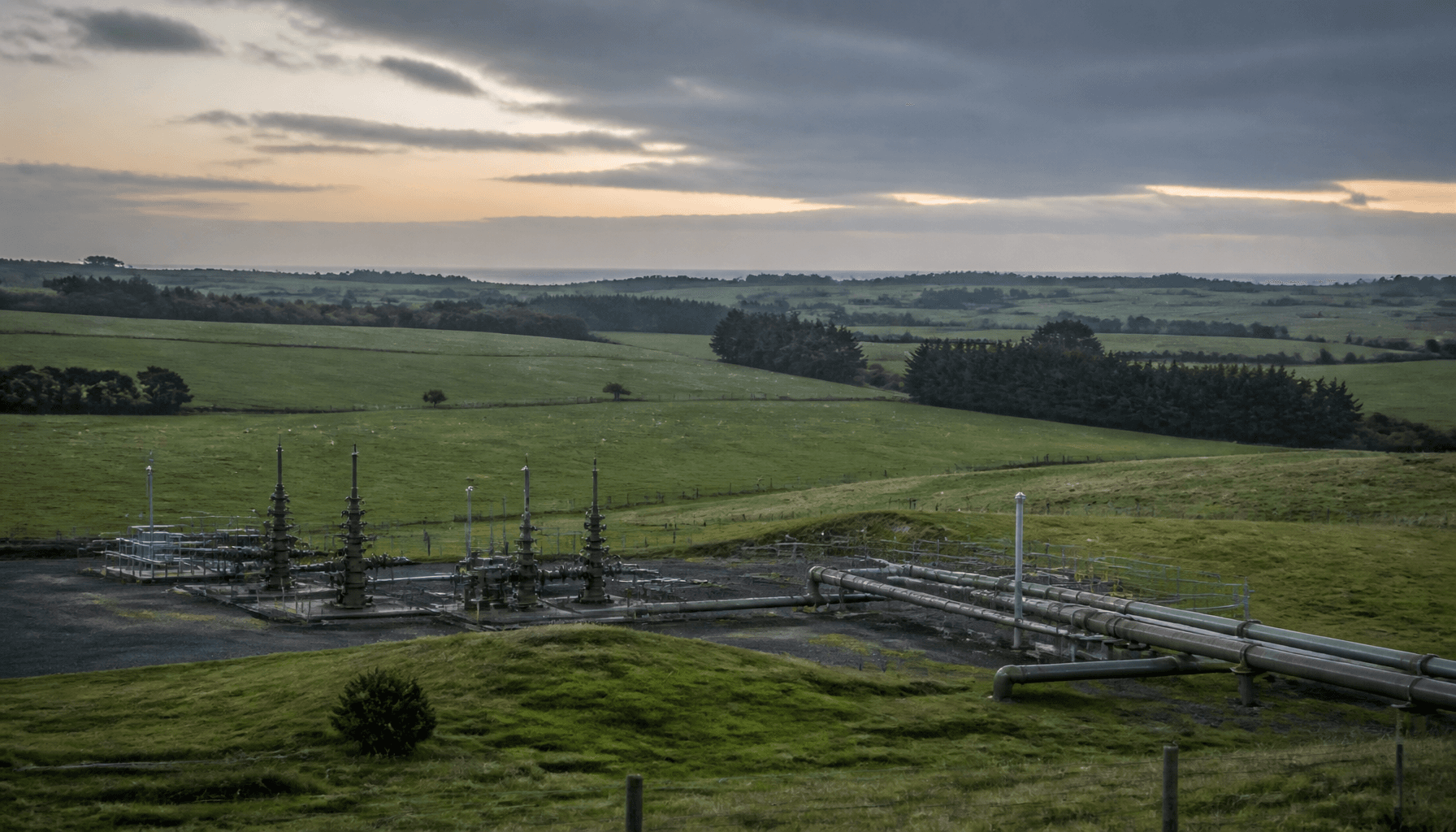 Gas storage wellhead infrastructure amid Taranaki farmland at dusk